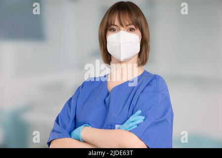 Porträt einer Ärztin oder einer Krankenschwester mit medizinischer Gesichtsmaske und medizinischen Handschuhen, die einen Operationsmantel vor einem Klinikraum tragen Stockfoto