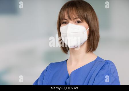 Porträt einer Ärztin oder einer Krankenschwester mit medizinischer Gesichtsmaske und medizinischen Handschuhen, die einen Operationsmantel vor einem Klinikraum tragen Stockfoto