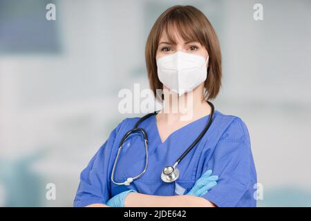 Porträt einer Ärztin oder einer Krankenschwester mit medizinischer Gesichtsmaske und medizinischen Handschuhen, die einen Operationsmantel vor einem Klinikraum tragen Stockfoto