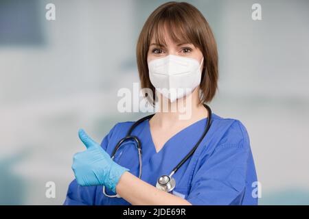 Ärztin oder Icu-Krankenschwester mit medizinischer Gesichtsmaske und medizinischen Handschuhen zeigt Daumen nach oben Stockfoto