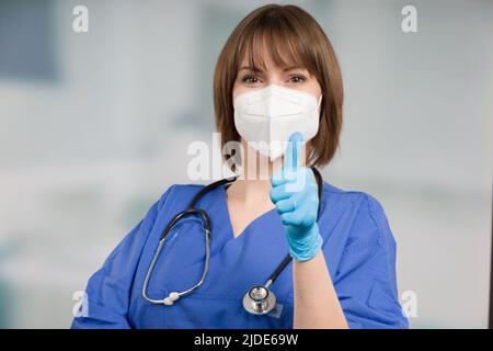 Ärztin oder Icu-Krankenschwester mit medizinischer Gesichtsmaske und medizinischen Handschuhen zeigt Daumen nach oben Stockfoto