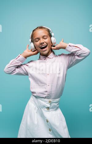 Positive Schulmädchen Musik in Kopfhörer isoliert auf blau hören Stockfoto