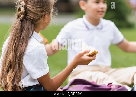 Präteen schulmädchen hält Sandwich in der Nähe verschwommen asiatische Freund im Park Stockfoto