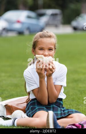 Schülerin hält Sandwich in der Nähe Gesicht auf Gras im Park Stockfoto