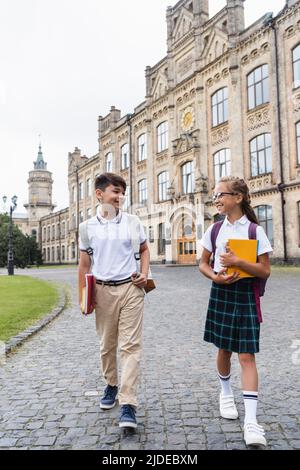 Positive multiethnische Schüler sprechen, während sie in der Nähe der Schule im Freien gehen Stockfoto