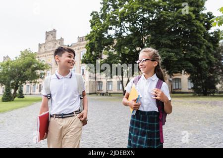 Positive interracial Schulkinder mit Notebooks zu Fuß im Freien Stockfoto