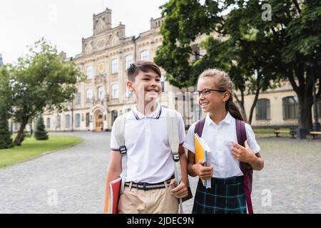 Lächelnde, multiethnische Schüler mit Notizbüchern, die im Freien laufen Stockfoto