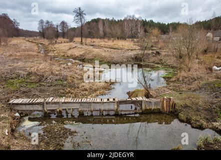 Alte zerbrochene hölzerne Fußgängerbrücke über den Fluss Ikva in der Westukraine. Stockfoto