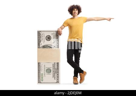 Junger Mann, der sich auf einen Geldstapel stützt und isoliert auf weißen Hintergrund zeigt Stockfoto