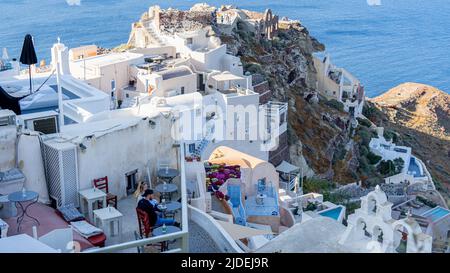 Ein Blick auf die steilen Terrassen der ikonischen Oia auf der Insel Santorini mit den Ruinen der Burg Agios Nikolaos im Hintergrund Stockfoto