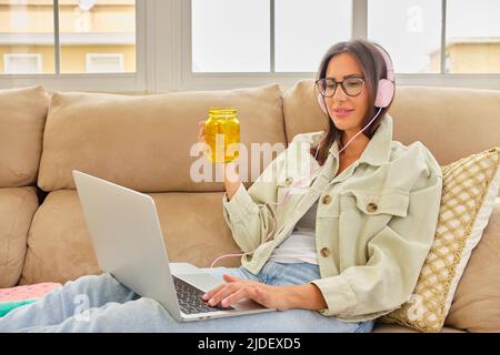 Konzentrierte tausendjährige Studentin in Brillen, die Lerncomputer liest, Glas mit frischem, reinem Wasser trinkt Stockfoto