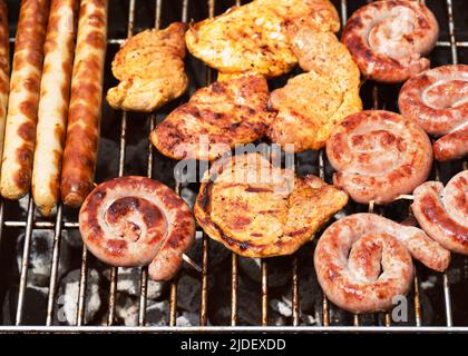 Verschiedene leckere gegrillte Fleisch über dem heißen Feuer auf einem tragbaren Grill mit Steaks, Würstchen, Huhn. Konzept für Grillparty oder Gartenparty im Sommer. Stockfoto