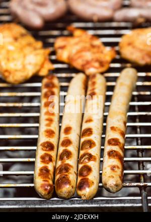 Leckere und leckere traditionelle deutsche Würstchen und Steaks über den heißen Kohlen. Grillparty oder Gartenparty im Sommer. Selektiver Fokus. Stockfoto