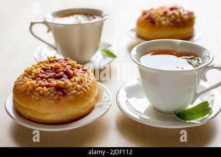 Süße Donuts auf Tellern und Tassen mit Minztee auf dem Holztisch. Leckeres Frühstück. Stockfoto