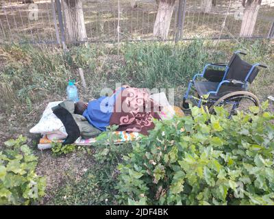 Obdachloser, der auf der Straße mit Rollstuhl-Hintergrund schläft. Stockfoto