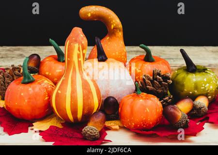 Auf Holzbrettern befinden sich Blätter verschiedener Schattierungen und Farben, Tannenzapfen, Eicheln und Kürbisse verschiedener Arten, Größen und Farben. Der Hintergrund i Stockfoto