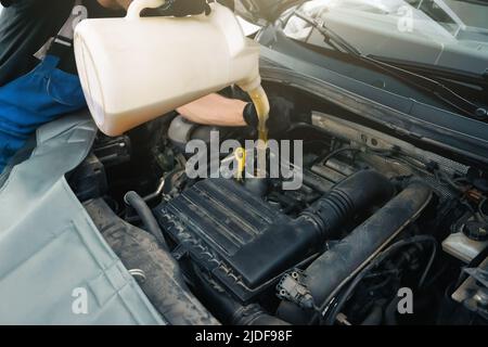Militärangehöriger, der Motoröl in den Motor in der Autowerkstatt eingießt, aus nächster Nähe. Stockfoto