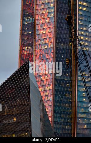 Die Glas- und Eisenfassade eines riesigen Wolkenkratzers bei Sonnenuntergang, Stahl, orange Farbe, Spiegelung der Sonne Stockfoto