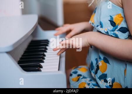 Kleines blondes Mädchen spielt zu Hause ein Spielzeug-Klavier. Musikalische Entwicklung in der Kindheit Stockfoto