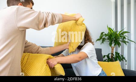 Ein paar von zwei glücklichen Freunden, die Spaß haben, zusammen auf dem Sofa zu Hause zu spielen und mit Kissen zu kämpfen genießen. Die Kissen waren morgens drinnen Stockfoto