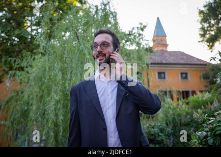 Junger Geschäftsmann in dunkler Jacke und weißem Hemd am Telefon mit einem Partner. Geschäftskonzept. Stockfoto