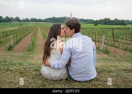 Junges verliebtes Paar sitzt auf dem Gras und küsst sich mitten auf dem Land. Liebeskonzept. Stockfoto