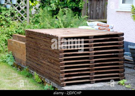Stapel von hölzernen Zaunplatten, Pfosten, Kiesbretter und Zementmischung, auf der Terrasse gelagert, bereit für den Ersatz des alten häuslichen Gartenzauens Stockfoto