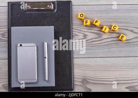 Klemmbrett mit Smartphone und Stift auf Holzschreibtisch. Flaches Bürowort aus Würfeln und Kopierraum. Stockfoto