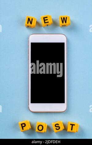 Smartphone mit gelben Buchstabenwürfeln mit neuen Post-Wörtern. Isoliert auf blauem Hintergrund. Stockfoto