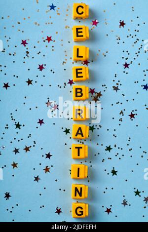 Vertikale Aufnahme von zelebrieren Wort aus gelben Buchstaben Würfel. Konfetti auf blauem Hintergrund. Draufsicht flach liegend. Stockfoto