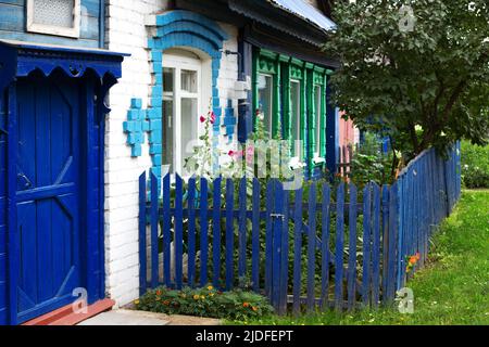 Altes Haus aus Holz und weißen Ziegeln mit grün geschnitzten Fensterrahmen, blauer Tür und vorderer Gartenzaun Stockfoto