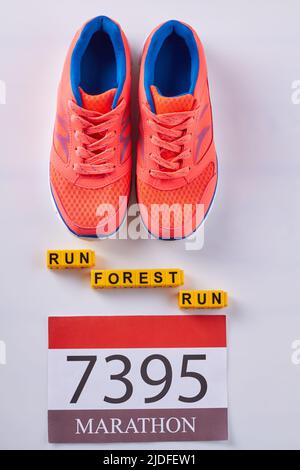 Flache, rote Sneakers mit Marathonnummer auf weißem Hintergrund. Vertikale Aufnahme, Draufsicht. Waldlauf. Stockfoto