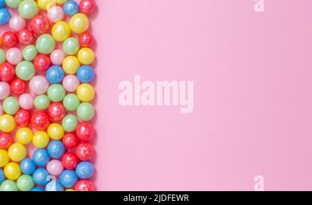 Mehrfarbige runde, glänzende Kugeln aus Zuckerkonditorei liegen links auf einem rosa Hintergrund. Stockfoto