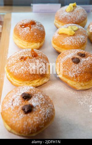 Donuts mit verschiedenen Geschmacksrichtungen, bestreut mit Puderzucker, in einer Bäckerei ausgestellt Stockfoto