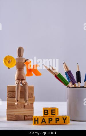 Still Life Holzfiguren mit einer Tasse Bleistiften. Gelbe Buchstabenwürfel in Be Happy Message angeordnet. Stockfoto
