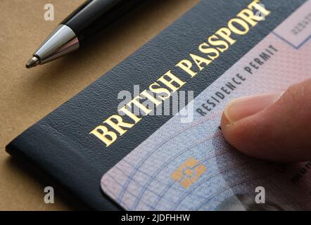 Finger zeigt auf die biometrische Aufenthaltserlaubnis (ILR, unbefristter Urlaub zu bleiben), die auf dem britischen Pass platziert wird. Konzept für die Einbürgerung. Stockfoto