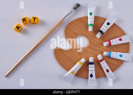 Draufsicht Pinsel mit Holzpalette und Ölrohren. Gelbe Buchstabenwürfel mit Wortkunst isoliert auf weißem Hintergrund. Stockfoto