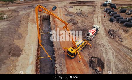 Schwere große Maschinen während der Straßenarbeiten. Ein gelber Kran füllt ein langes Loch mit frischem Zement. Hochwertige Fotos Stockfoto