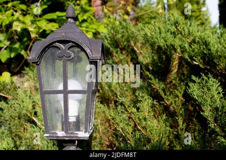 Schwarze Straßenlampe aus Eisen vor dem Hintergrund von Bäumen und blauem Himmel. Geschmiedete Details der Architektur. Stockfoto