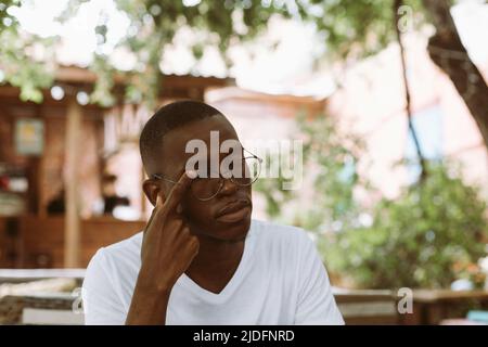 Erschöpfter Mann mit dunkler Haut, der die Brille auszieht, seine Augen berührt und reibt, Schmerzen im Freien spürt. Verschwommenes Sehproblem Stockfoto