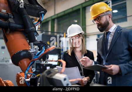 Chefingenieur und Projektleiter in moderner Industriefabrik mit Roboterarmen reden und planen Optimierung der Produktion. Stockfoto