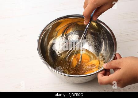 Geschlagene Eier auf Edelstahlschüssel mit Baloon-Whisk. Prozess Backen Kuchen Rezept, Lebensmittel Fotografie Idee Konzept Weiß Luftig Helle Stimmung Stockfoto