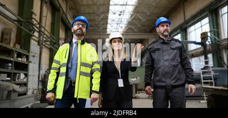 Manager Supervisoren und Industriearbeiter in Uniform zu Fuß in große Metallfabrik Halle und sprechen. Low-Angle-Ansicht. Stockfoto