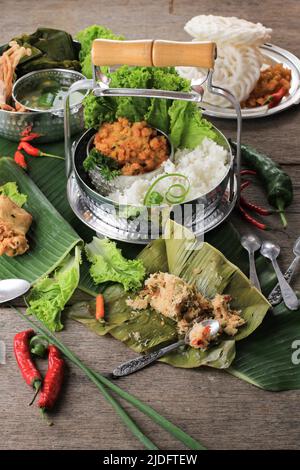Traditionelle indonesische Gerichte für Tagesmenüs, serviert mit Rantang (stapelbare Reiskiste). Weißer Reis, Spinatsuppe, Maisfritter, Bothok Mlandingan und Stockfoto