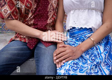 Die Hand des Mannes streichelte den Arm seines Transgender-Partners, der vor einem Tempel saß Stockfoto