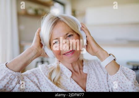Ältere Frau mit Kopfhörern, die zu Hause Entspannungsmusik hört Stockfoto