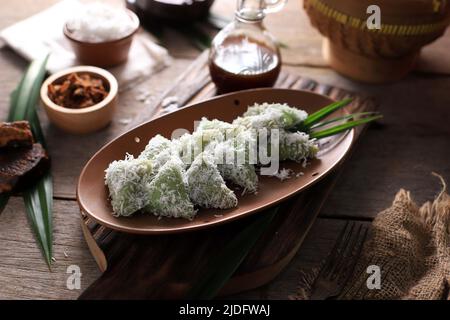 Lupis, indonesischer traditioneller Snack aus klebriges Reis, verpackt mit Bananenblatt, Shape Triangle serviert mit flüssigem Palmzucker und geriebener Kokosnuss Stockfoto