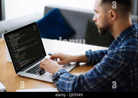 Softwarekonzept. Seitenansicht des intelligenten kaukasischen IT-Spezialisten, Programmierer, sitzt zu Hause, nutzt Laptop, konzentriert auf die Entwicklung einer Website, Anwendung, Schreiben von Codes und Datencode Stockfoto