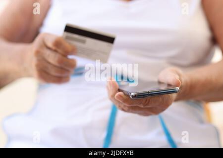 Nahaufnahme einer alten Frau, die Mobiltelefon und Bankkarte in den Händen hält. Ältere Frauen, die elektronische Zahlungen leisten. Pensionsfonds- und Zahlungskonzept Stockfoto
