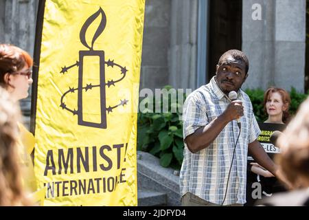 Mamadou KonatÈ, ein Flüchtling aus der Elfenbeinküste, der in vier Haftanstalten in Quebec festgehalten wurde und seine Asylanträge während des Protestes abgelehnt hatte, spricht. An diesem Weltflüchtlingstag organisierte Amnesty International Canada in Zusammenarbeit mit Human Rights Watch einen Protest vor dem Büro des Premierministers Ministerís in Montreal, um das Ende der eingeleiteten Haft von Flüchtlingen und Asylbewerbern in Quebec zu fordern. Die Kampagne mit dem Namen #BienvenueAuCanada suchte nach Unterschriften von Quebecís-Politikern, um Verträge mit Provinzgefängnissen zu beenden, die Migranten aufnehmen. Stockfoto